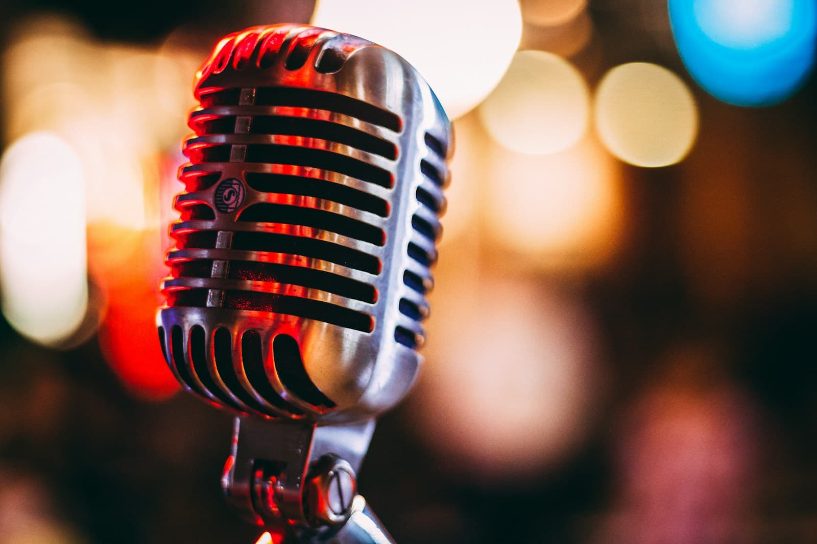 A chrome vintage microphone in sharp focus against blurred warm and blue stage lights