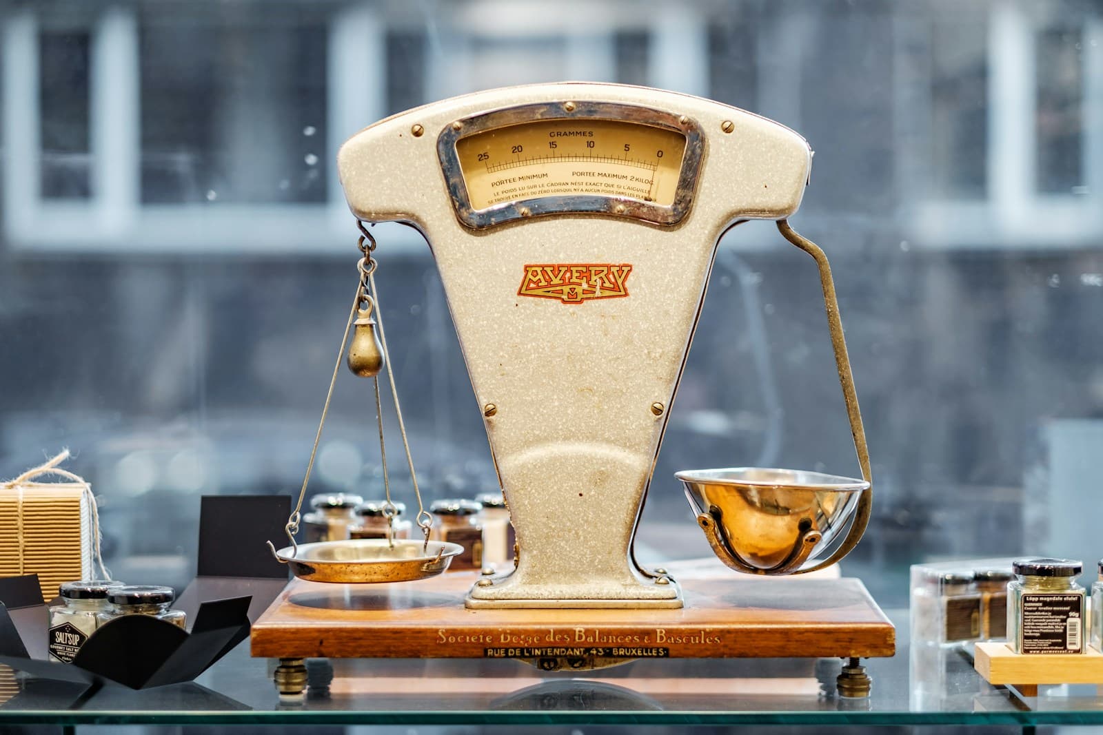 A vintage Avery balance scale on a wooden base, displayed in a shop window with small jars beside it