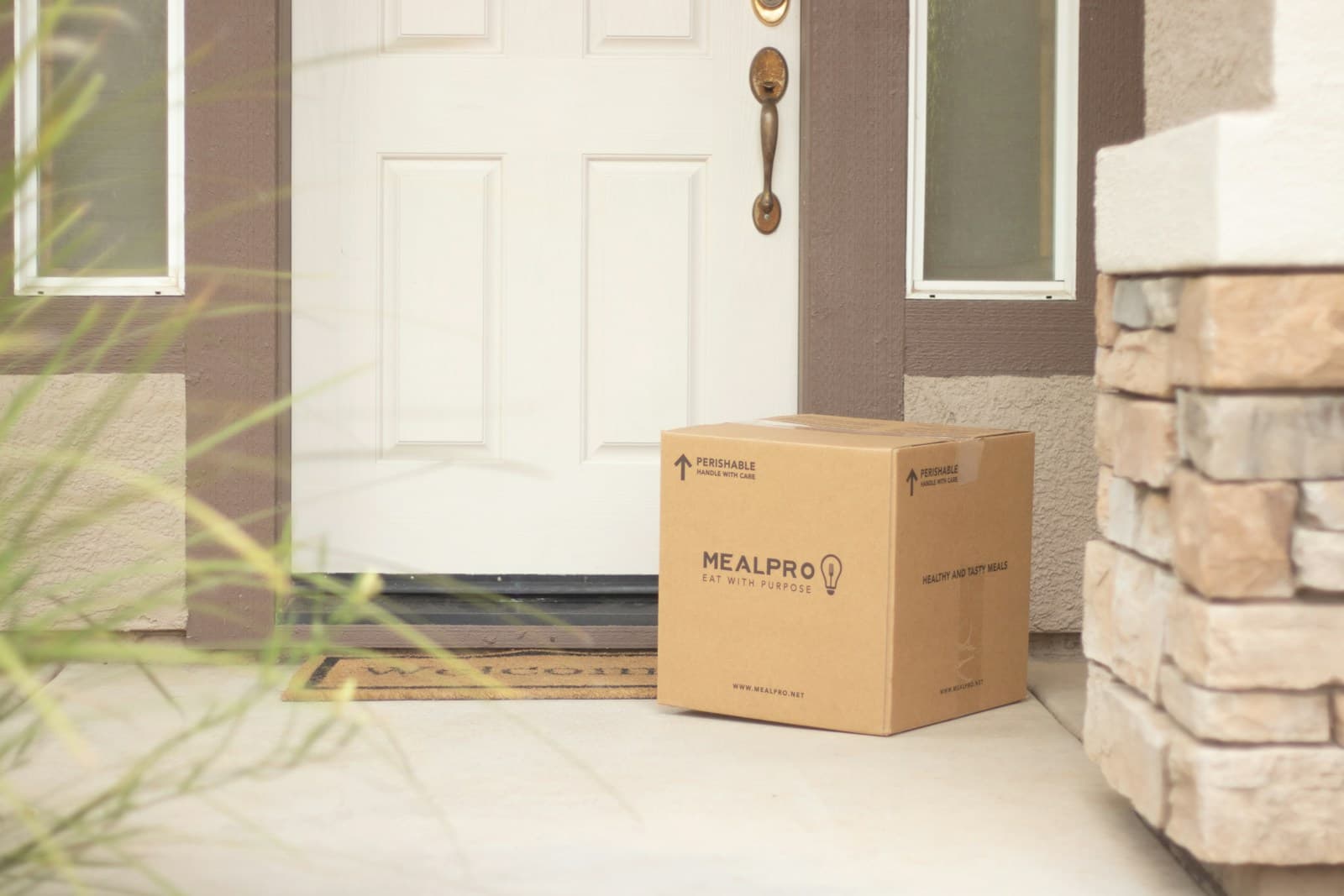 A cardboard box delivered on a doorstep next to a welcome mat in front of a white front door