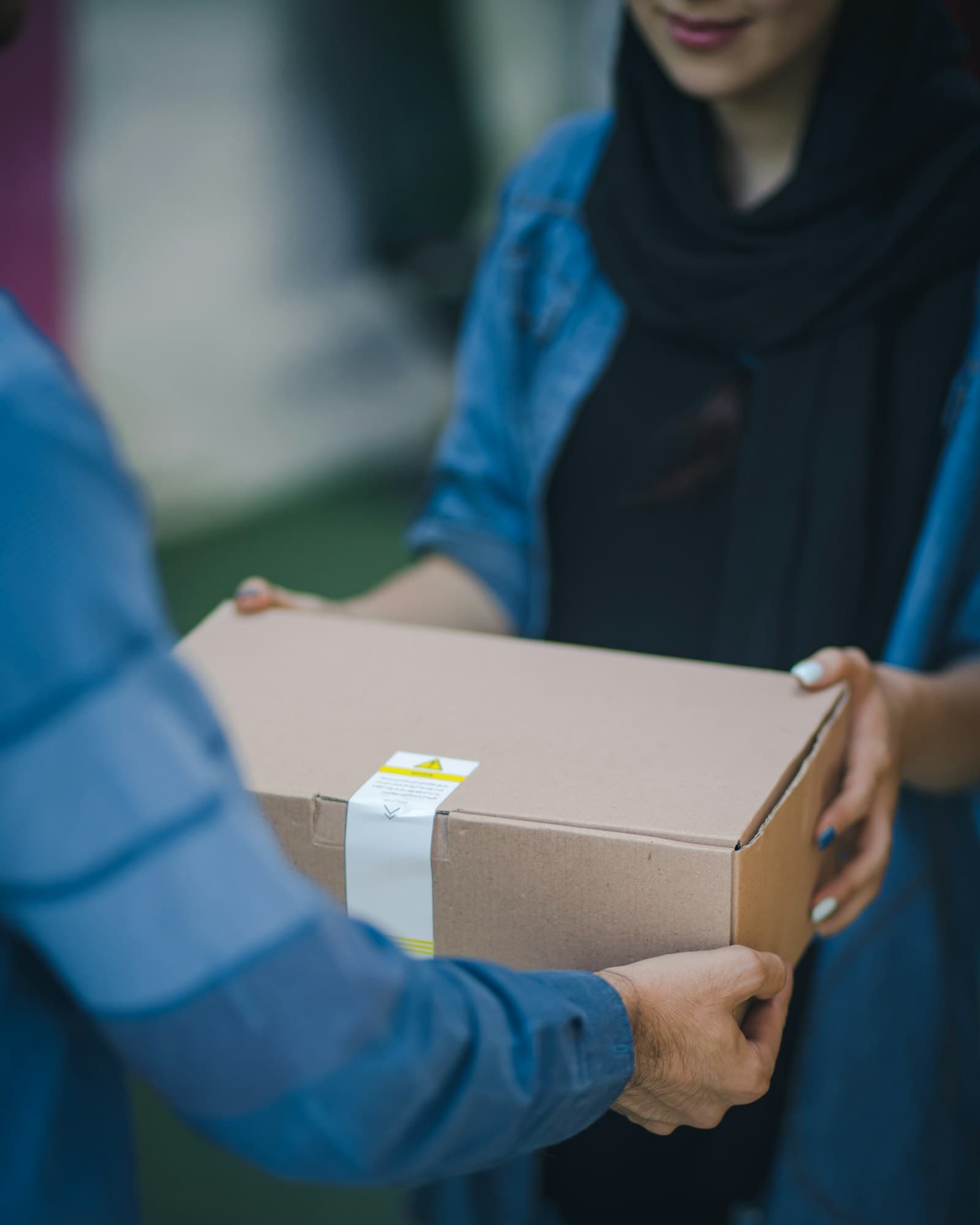 A courier in a blue jacket handing a sealed cardboard parcel to a customer