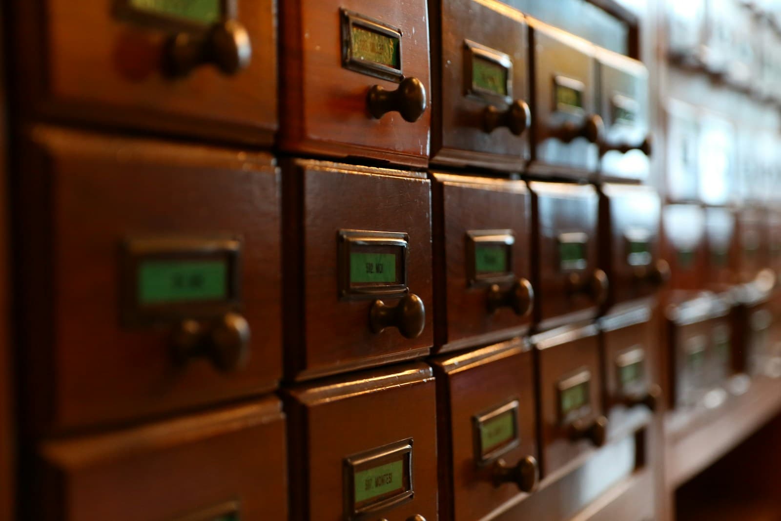Rows of wooden library card-catalogue drawers with small labelled brass handles, photographed at an angle