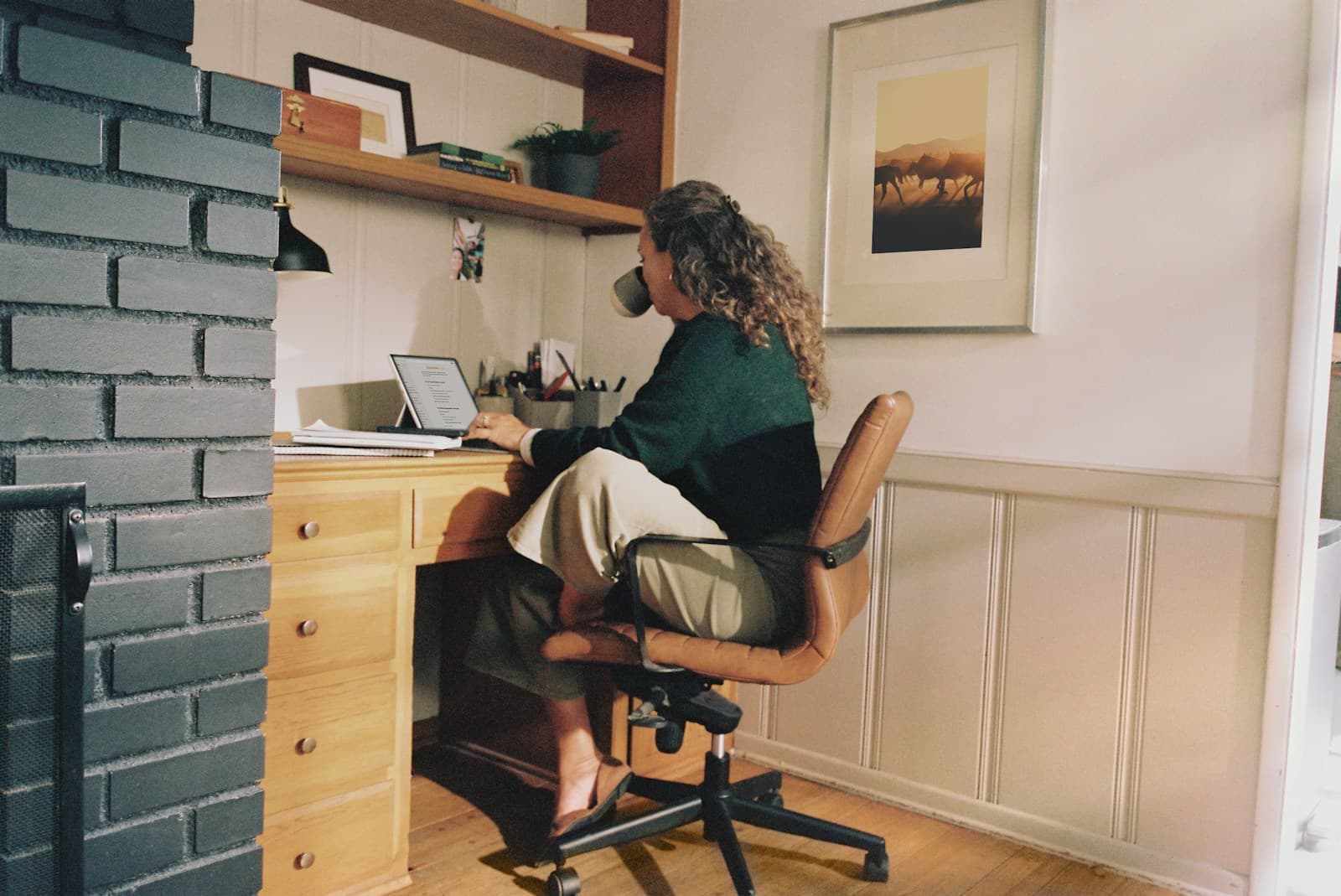 A person at a home office desk reading a checklist on a laptop while drinking coffee, reviewing chatbot answers