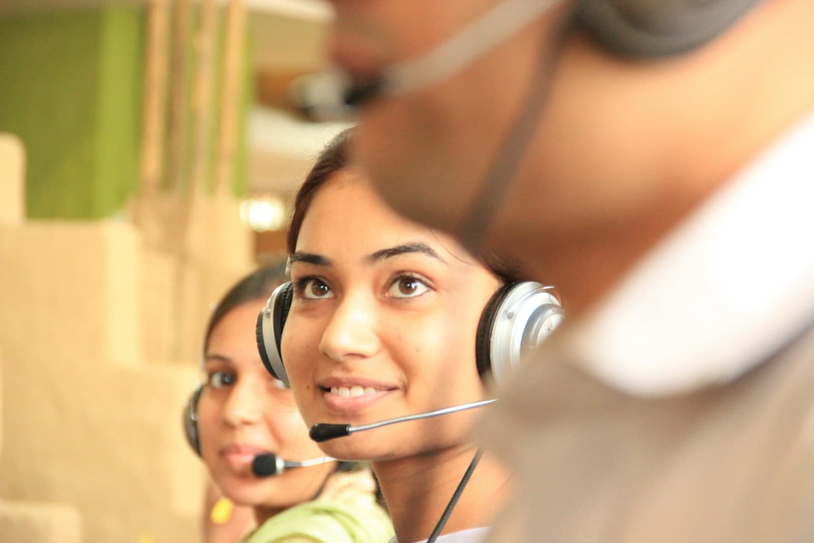 Smiling customer support agents wearing headsets at their desks in a busy office