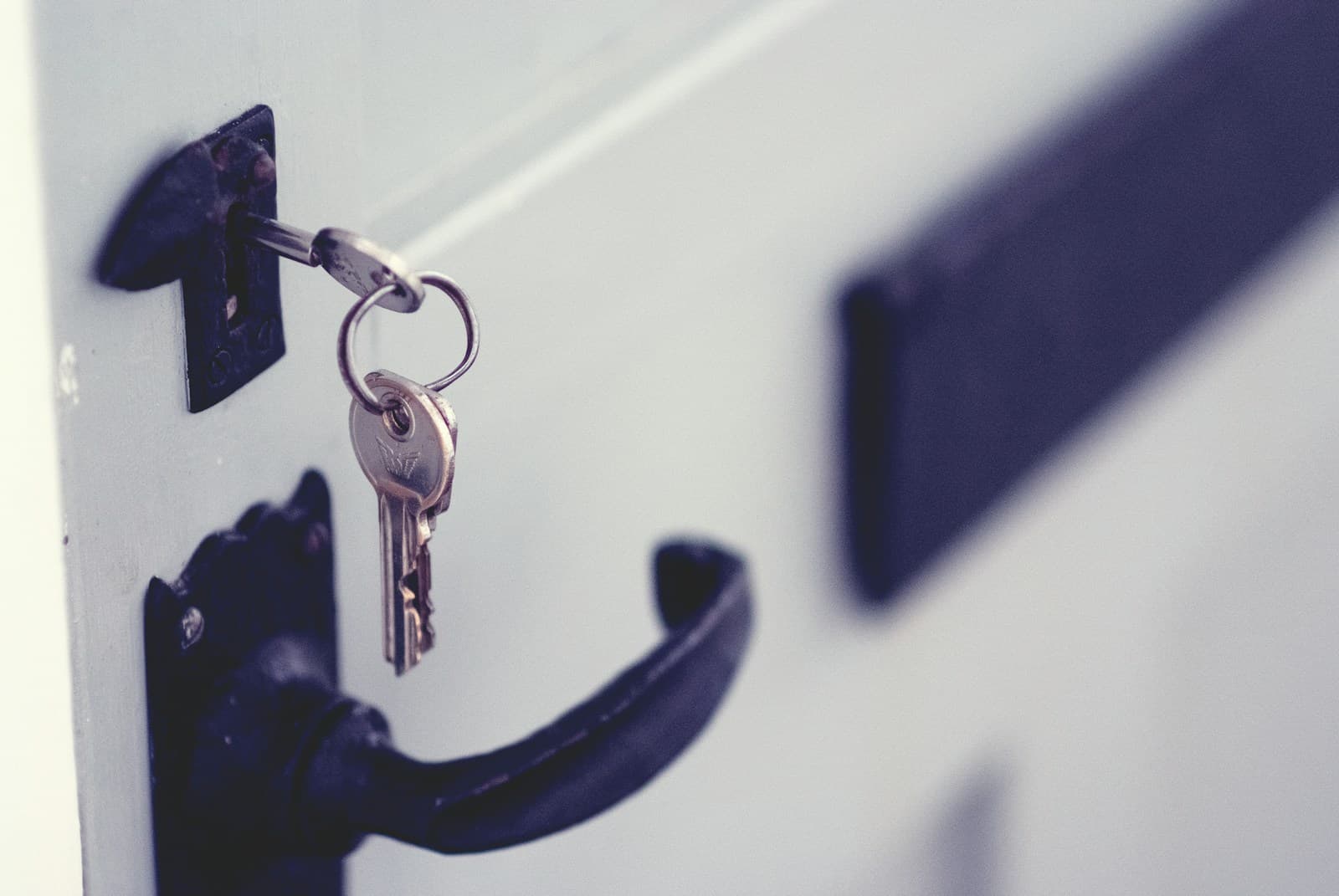 A bunch of keys hanging from a lock in a pale wooden door, with the door handle below