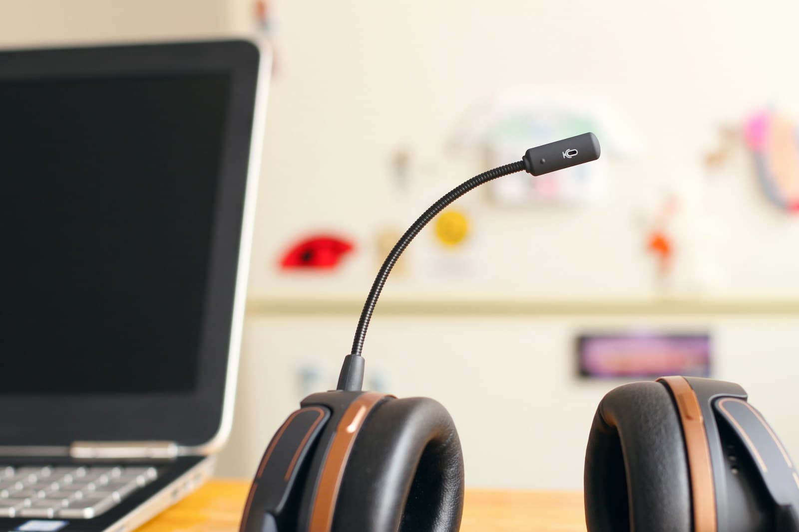 A black headset with a boom microphone resting on a wooden desk next to an open laptop